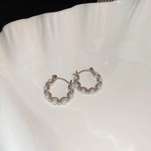 Silver wavy hoop earrings with small pearls on a white shell tray minimalist style