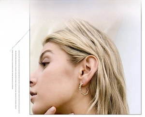 Detail of twisted rope design gold C-shaped earrings worn by a model in a close-up view