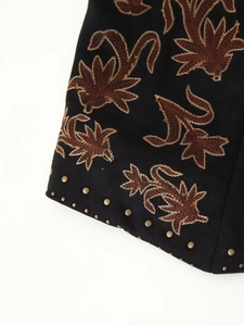 Détail de la broderie florale ethnique et des rivets dorés sur le gilet en daim noir