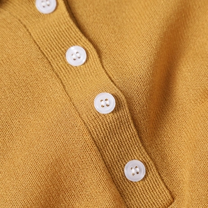 Macro shot of mustard yellow knit polo shirt detailing texture and white buttons