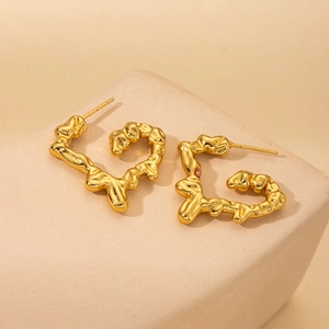 Macro view of gold-plated irregular liquid heart earrings on textured stone base