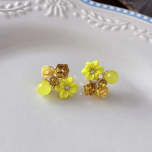 Close-up of yellow floral stud earrings with opal cat eye stone and crystal on ceramic