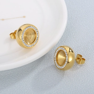 Elegante goldene runde Zirkon-Ohrstecker auf einem weißen Keramikteller vor grauem Hintergrund