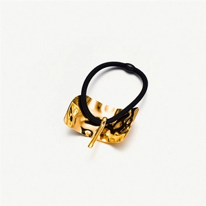 Detail of black elastic hair tie with a textured gold irregular metal plate embellishment