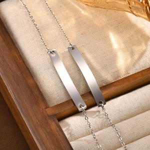 Detail view of two minimalist stainless steel bar necklaces on a linen display stand
