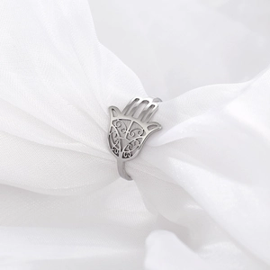 Macro view of silver stainless steel Hamsa Hand ring nestled in soft white silk fabric