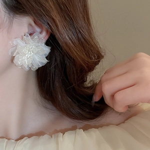 Close-up of a white lace flower earring with faux pearl center on a model