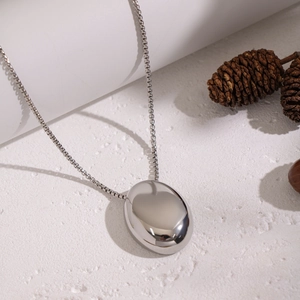 Vue détaillée du pendentif ovale argenté avec chaîne gourmette sur surface texturée