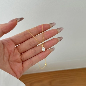 Macro detail of a golden necklace with an oval transparent gemstone held by hand
