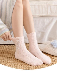 Close-up of pink coral fleece thermal socks with bow knots on feet in home setting