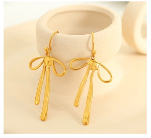 Macro shot of gold bow tassel earrings with polished metallic finish on ceramic base