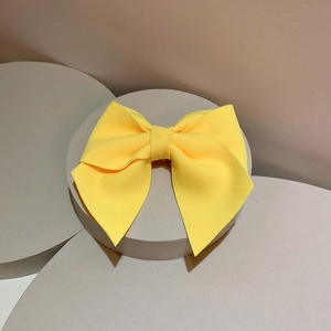 Detail of bright yellow bow hair clip with ribbed texture on a gray display stand