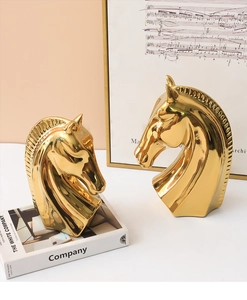 Dettaglio di due sculture a testa di cavallo dorate con finitura a specchio sul tavolo