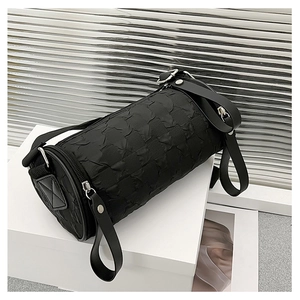 Detail of black cylindrical crossbody bag featuring embossed pleated texture and silver hardware