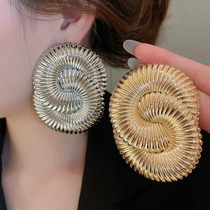 Detailed close-up of oversized geometric spiral textured hoop earrings in gold and silver