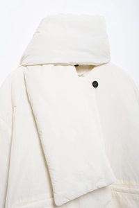Detailaufnahme der weißen Steppjacke mit gestepptem Stoff und schwarzem Knopfverschluss