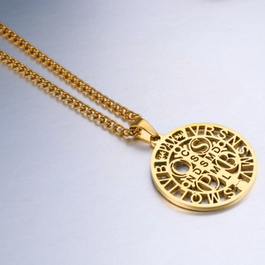 Close-up of golden Saint Benedict medal with intricate hollow lettering on Cuban chain