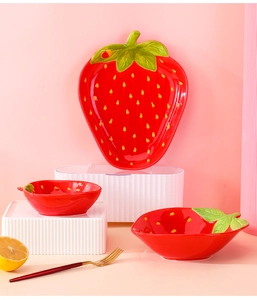 Detailed close-up of ceramic strawberry-shaped plates and bowls on a pink backdrop
