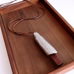 Detail of vintage geometric metal pendant with textured wood inlay on brown cord