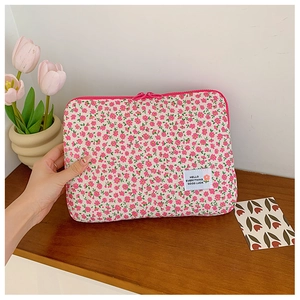 Pink floral quilted laptop sleeve with zipper closure and white woven label on desk
