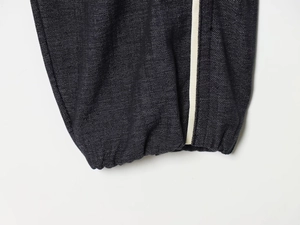Détail d'un pantalon en jean foncé avec bandes latérales blanches et chevilles élastiques