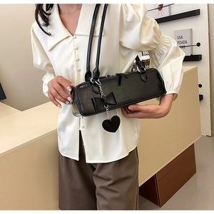 Detail of black glossy cylindrical baguette bag with bow and heart chain on model
