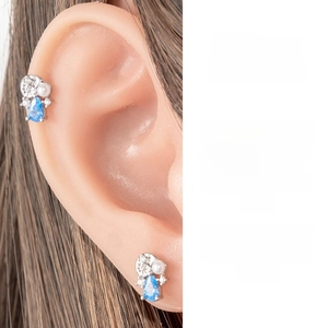 Detail of silver piercing stud featuring a blue teardrop zircon and white pearl accent