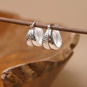 Macro detail of silver textured hoop earrings featuring a unique cocoon-like vertical pattern