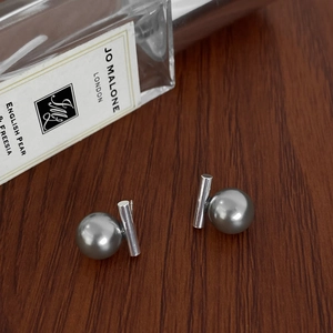 Close-up of minimalist pearl stud earrings on wood with perfume bottle backdrop