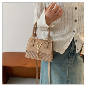 Detail of light khaki shoulder bag featuring a gold V-shaped logo and elegant tassel