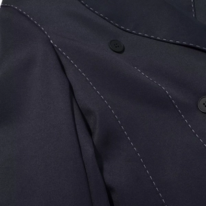 Dettaglio delle cuciture bianche a contrasto e bottoni neri su blazer blu navy a trama