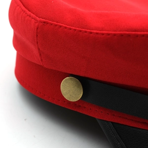 Detailed close-up of red twill fabric with black leather trim and brass button