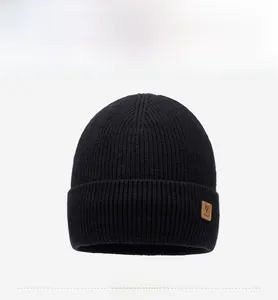 Close-up of black knitted winter beanie with brown leather patch and folded cuff edge