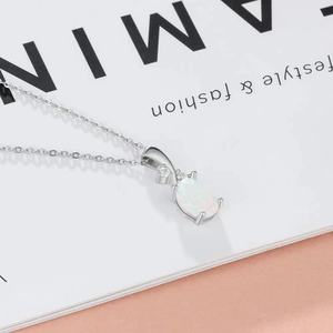 Close-up of silver oval opal pendant necklace with zircon accents on a magazine
