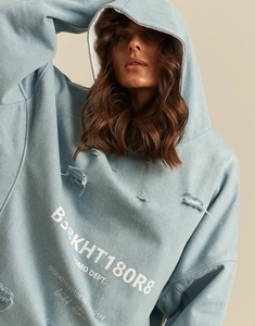 Detail of light blue denim hoodie with distressed ripped texture and white text print