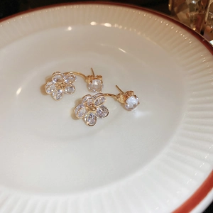 Macro shot of gold floral earrings with crystal petals on a white ceramic plate