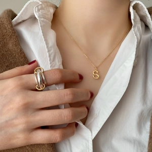 Close-up of golden S-letter necklace and bicolor multi-layered ring on female model
