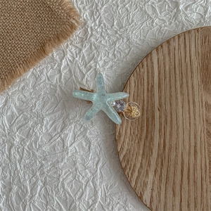 Close-up of a blue starfish hair clip with pearl and crystal ball on a white paper background