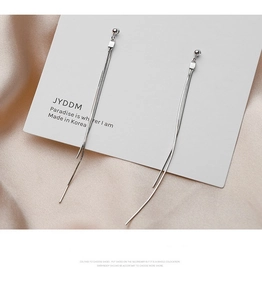 Detailed macro shot of silver tassel drop earrings on elegant champagne satin fabric