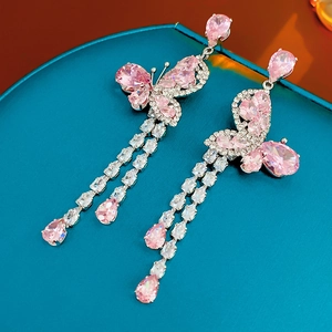 Macro shot of silver tassel earrings with pink butterfly zircons on a textured background