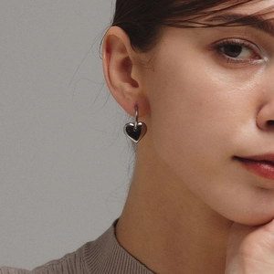 Close-up of model wearing silver 3D heart drop earrings with a polished metallic finish
