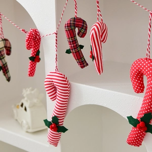 Weihnachtsanhänger in Zuckerstangenform mit Karomuster und roten Beeren an weißer Wand