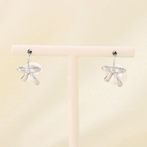 Detailed view of silver bow earrings with white pearl pendants on a pink stand