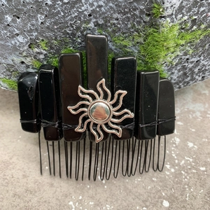 Natural black crystal hair comb with silver sun charm on a mossy stone background