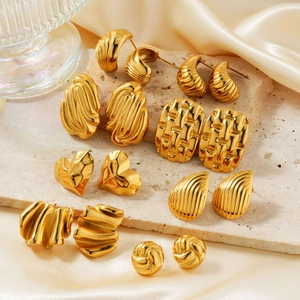 Collection of geometric gold stainless steel earrings on a beige stone and silk background