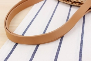 Detail of light brown faux leather shoulder strap on a woven paper straw beach bag