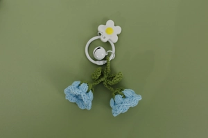 Close-up of handmade blue knitted lily of the valley pendant with white bell charm