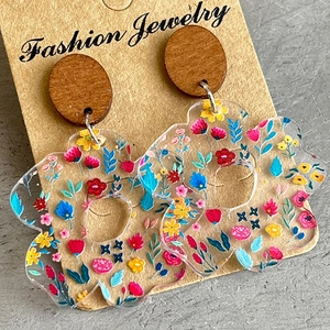 Macro view of floral pattern acrylic earrings with round wooden studs on craft card