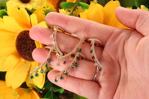 Dettaglio di ear cuff dorati con zirconi e nappe colorate con taglio a pera