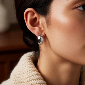 Detailed view of silver hoop earring with quilted texture worn by model for elegant style